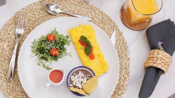 A plate with a rolled omelette, a salad, and a bowl of beans with chips.