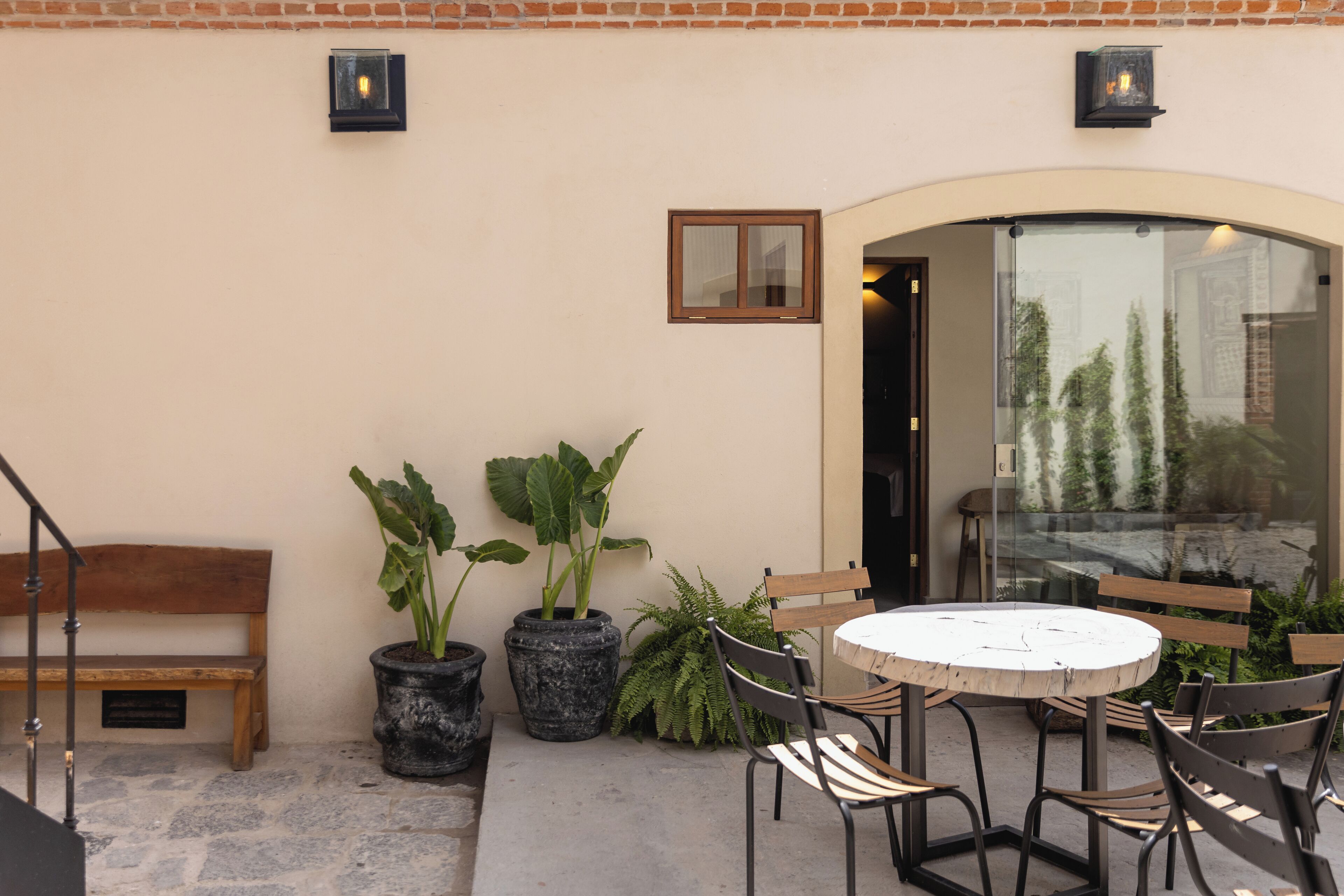 Une terrasse extérieure avec une table ronde et des chaises, un banc en bois et des plantes en pot.