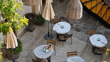 Ein Terrassenbereich im Freien mit runden Tischen und Stühlen, umgeben von Blumentöpfen und hängenden Korbuschirm