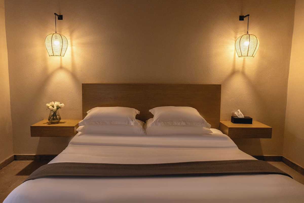 Una habitación de hotel con una cama grande, dos mesitas de noche y dos lámparas fijadas a la pared.