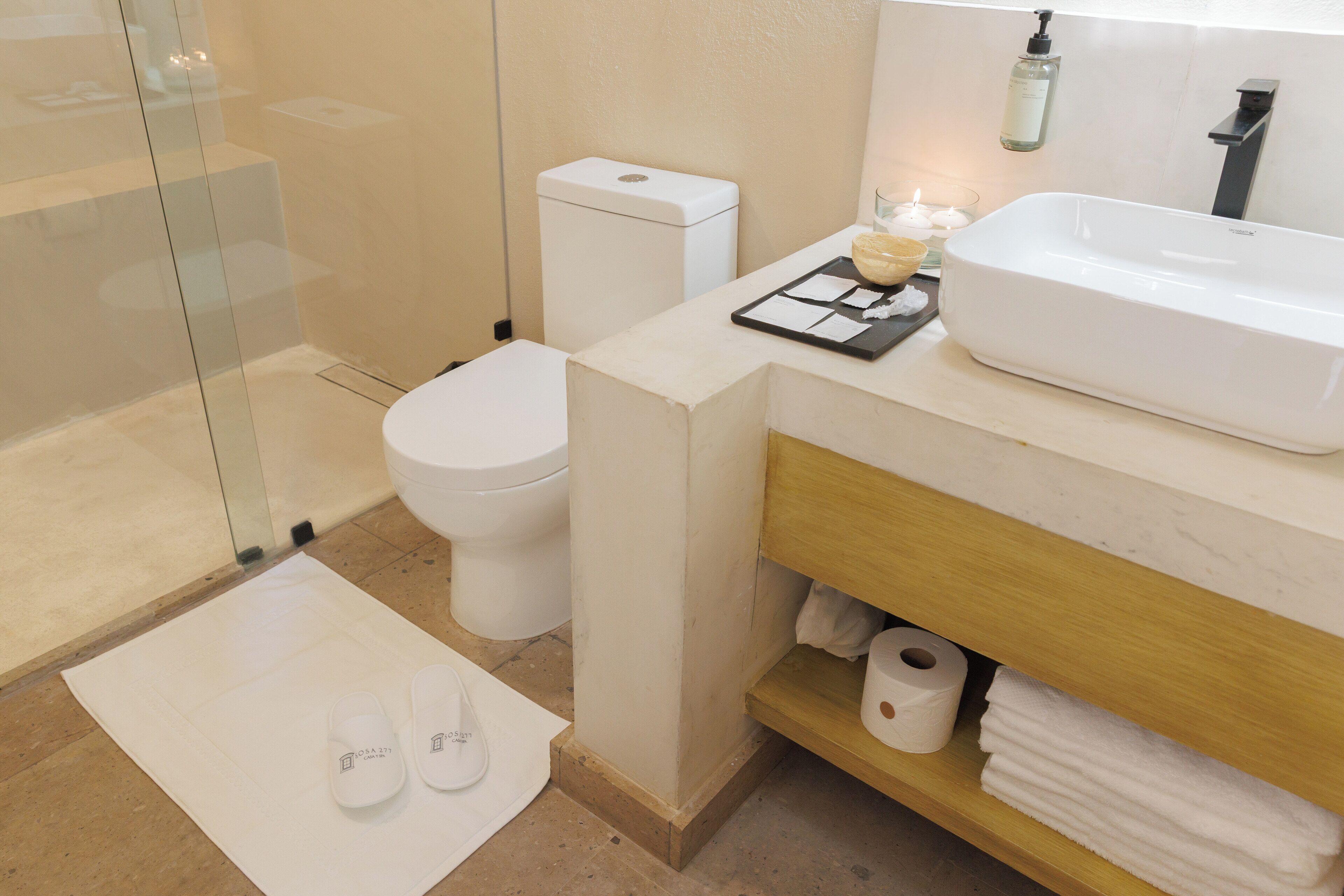 A modern bathroom with a glass shower enclosure, a white toilet, a sink with a soap dispenser, and a towel rack.