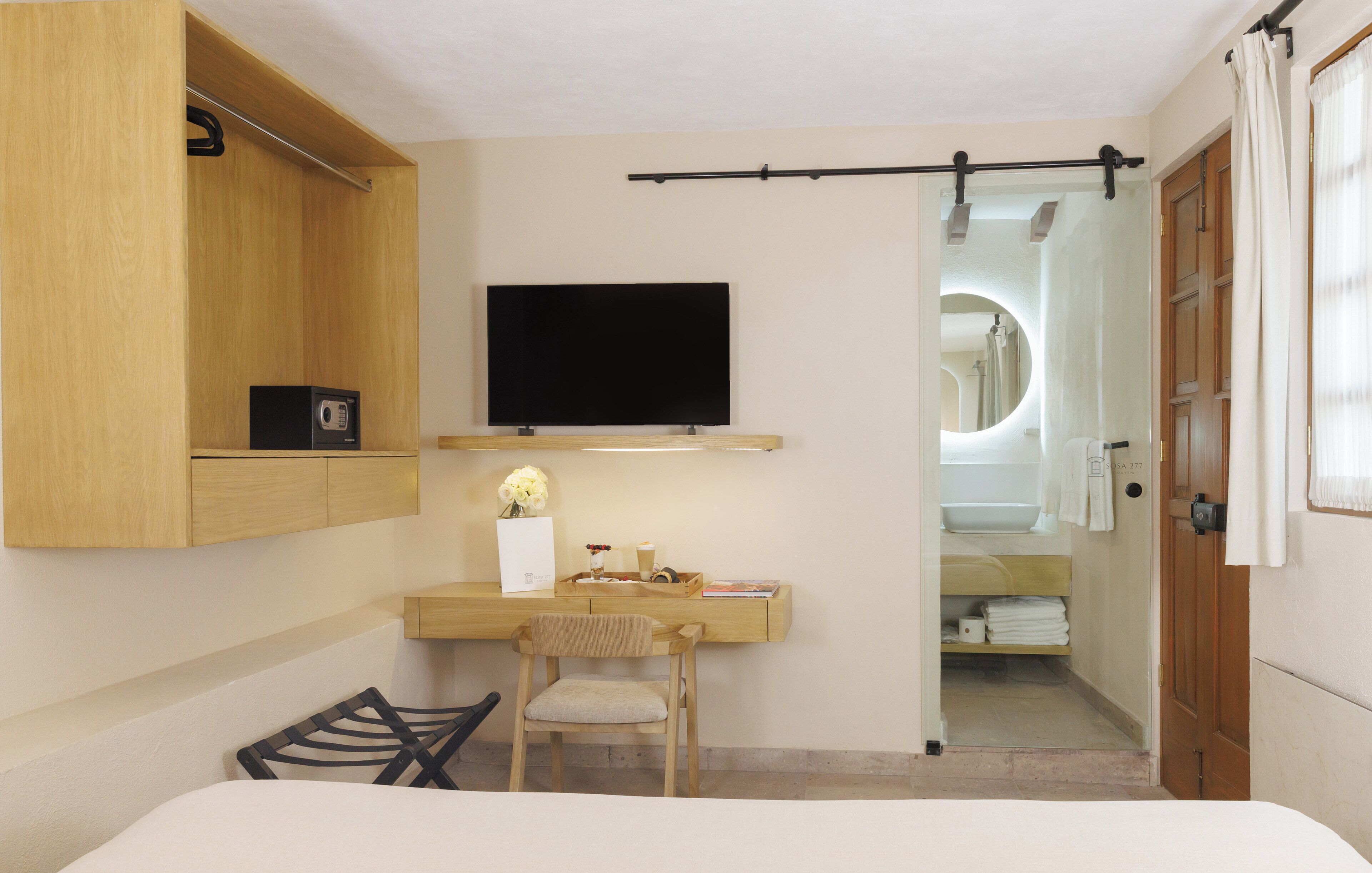 Een kleine hotelkamer met een houten bureau, een wandtelevisie, een stoel en een bed.