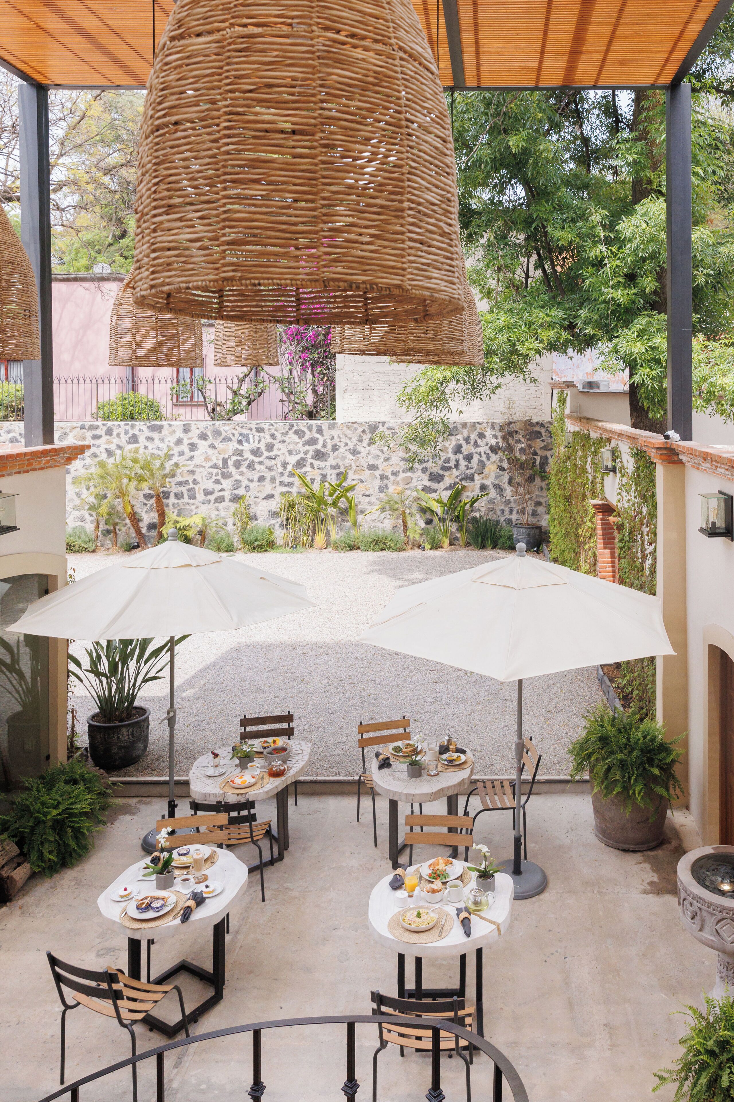 Une terrasse extérieure avec des tables et des chaises rondes, entourée de plantes en pot et d’un mur de pierre.