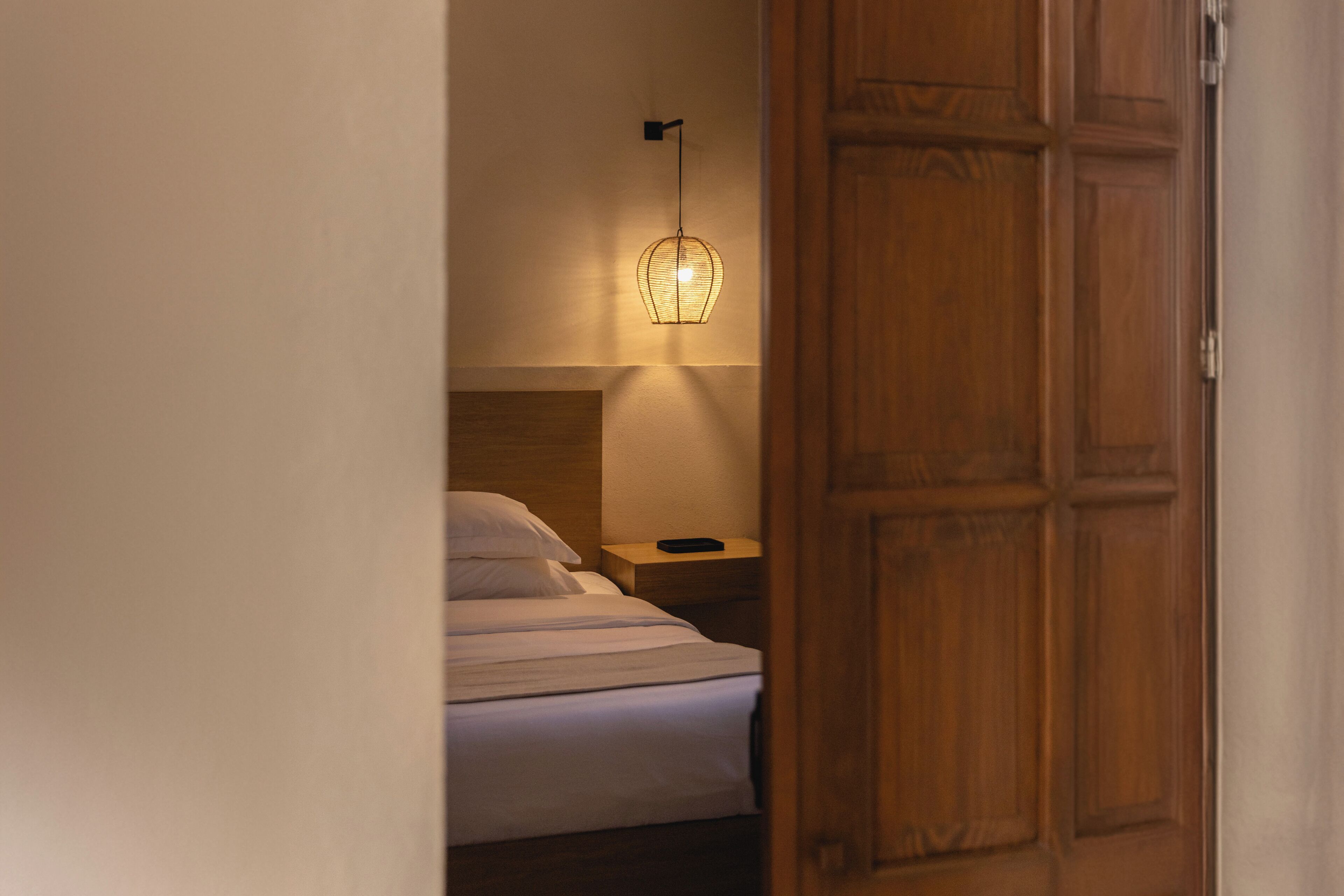 A bedroom with a bed, bedside table, lamp, and wooden door.