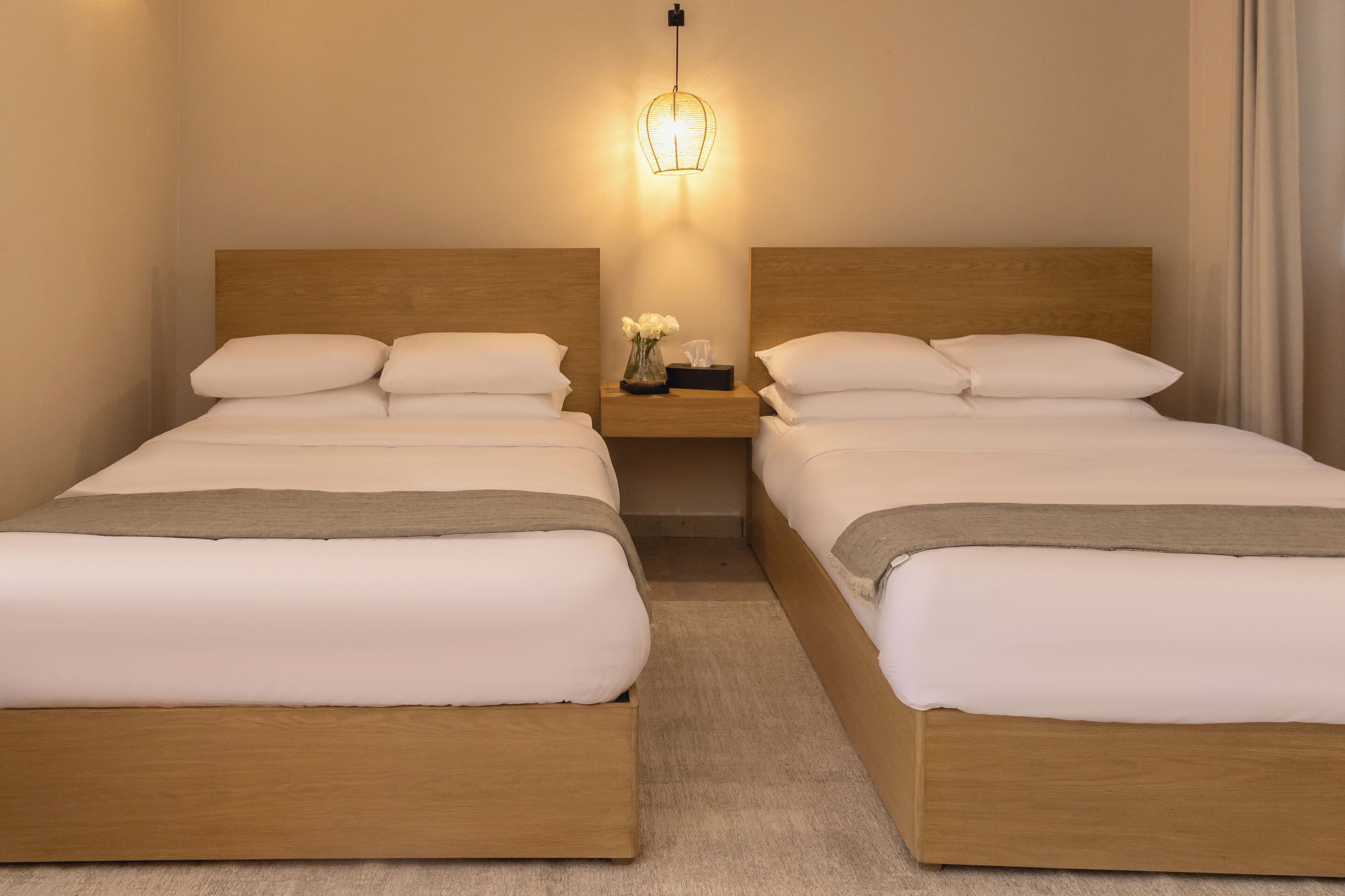 Una habitación doble con dos camas, una mesita de noche con lámpara y un jarrón con flores.