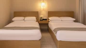 Una habitación doble con dos camas, una mesita de noche con lámpara y un jarrón con flores.