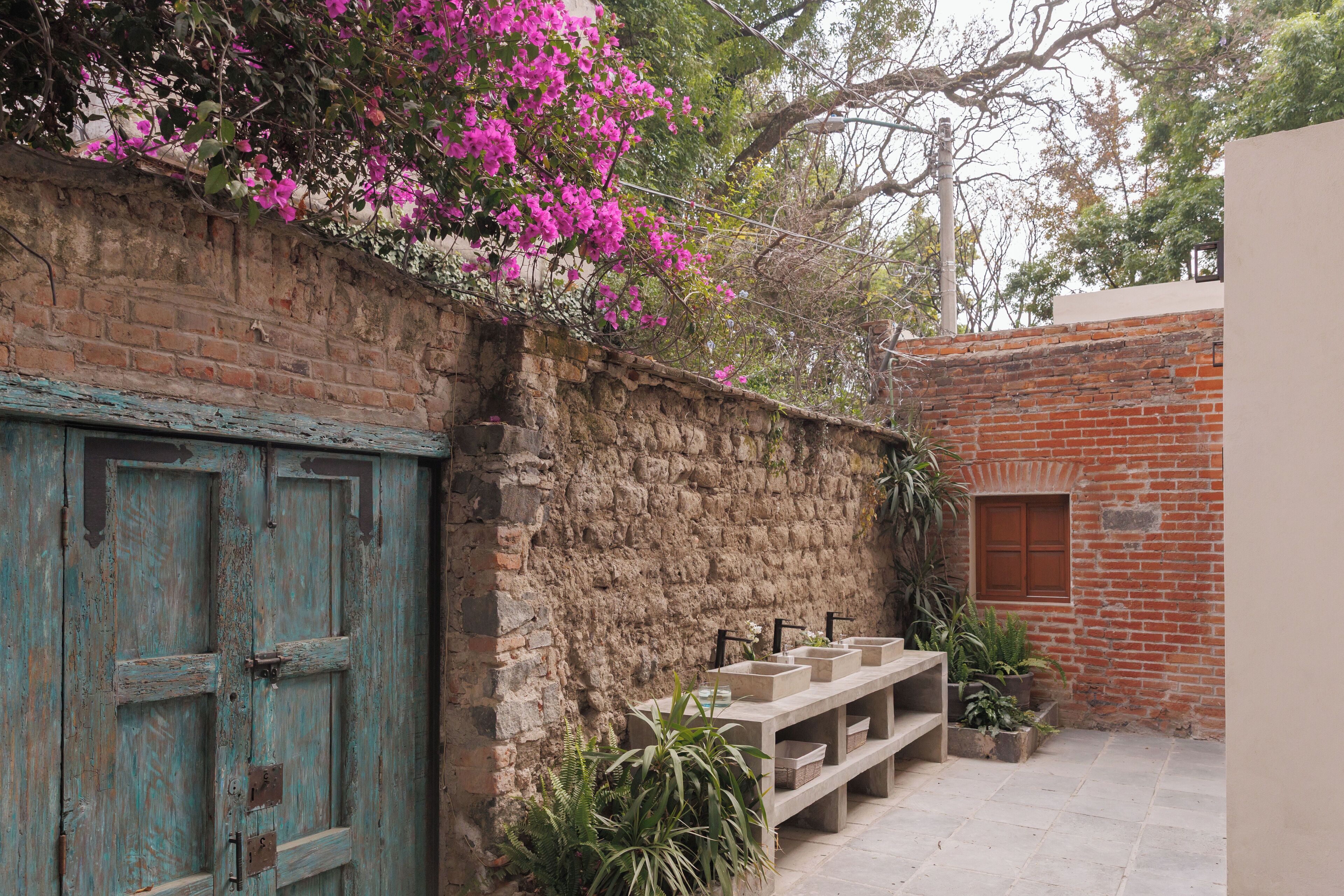 A rustic courtyard with a weathered blue door, a stone wall, and a brick building.