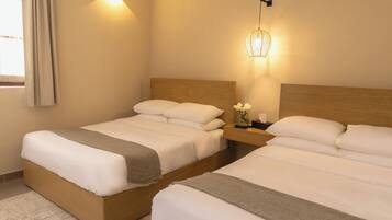 Habitación de hotel con dos camas, una mesita de noche, un aplique en la pared y un ventanal con cortinas.