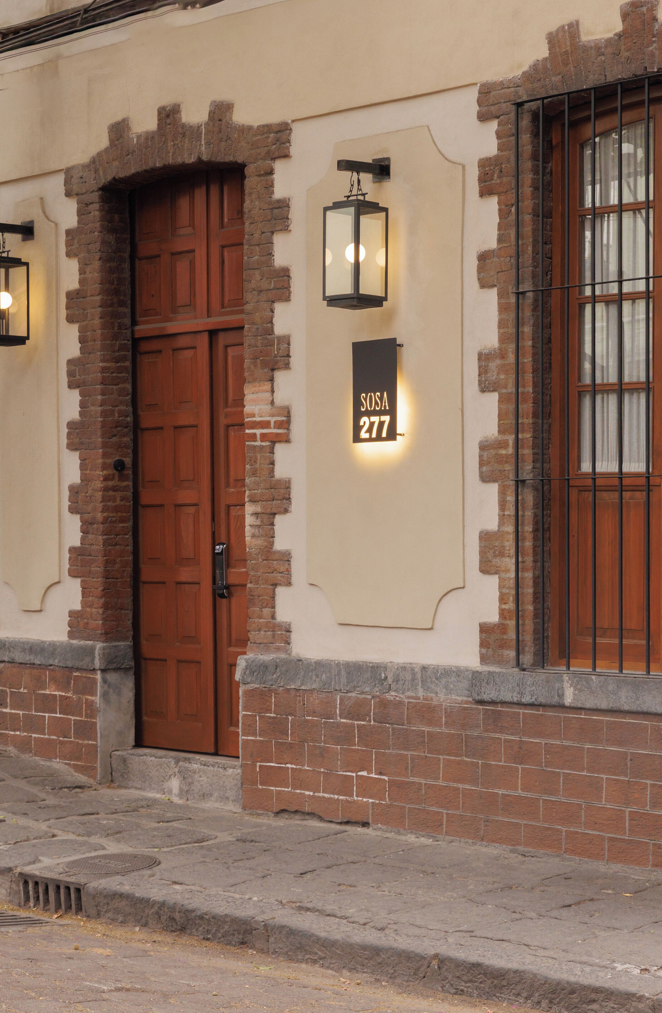 A building with a brown wooden door, a sign reading "SOSA 277", and a lantern-style light fixture.