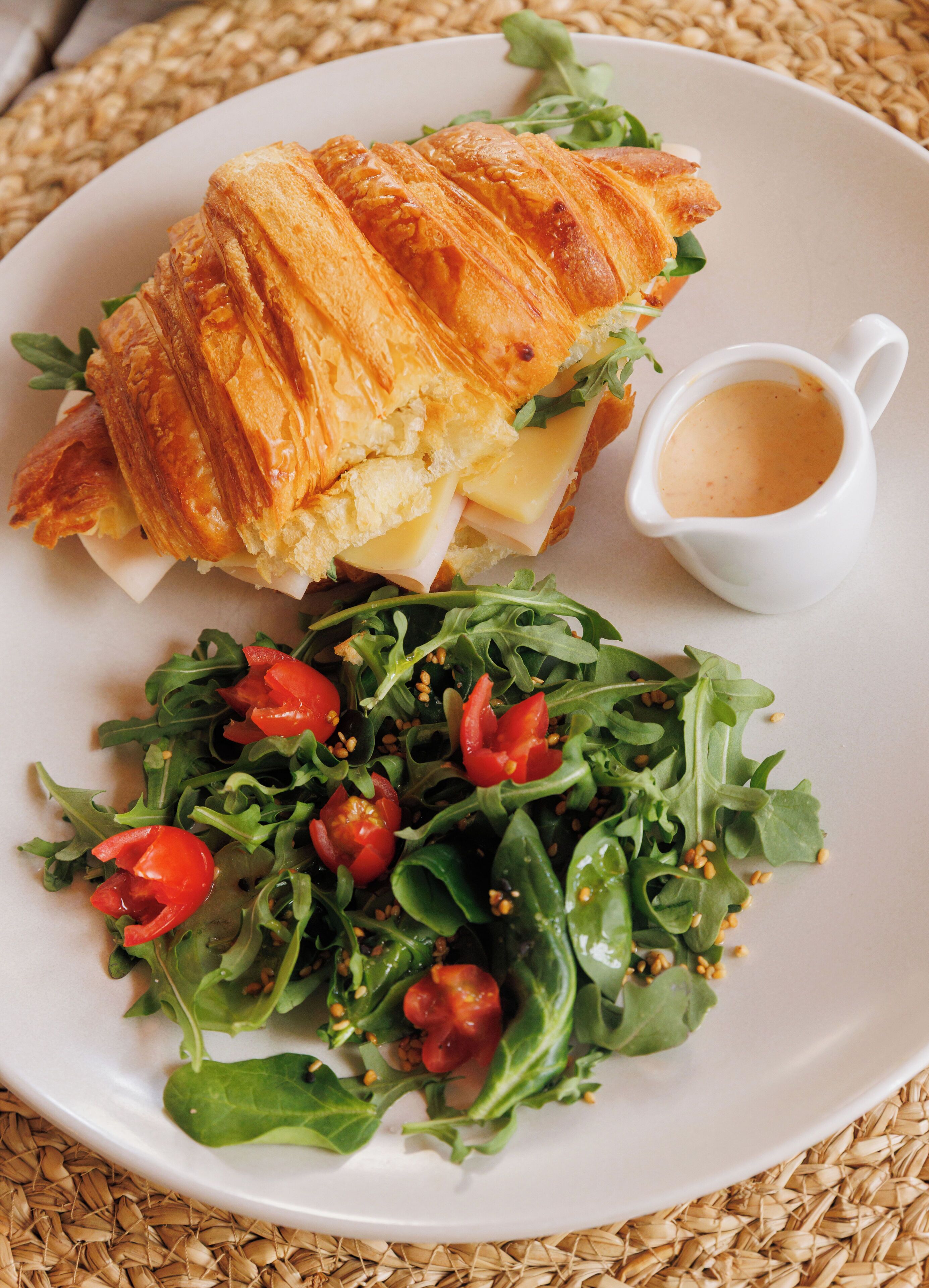 En tallerken med en croissant-sandwich, en lille kop sauce og en salat.