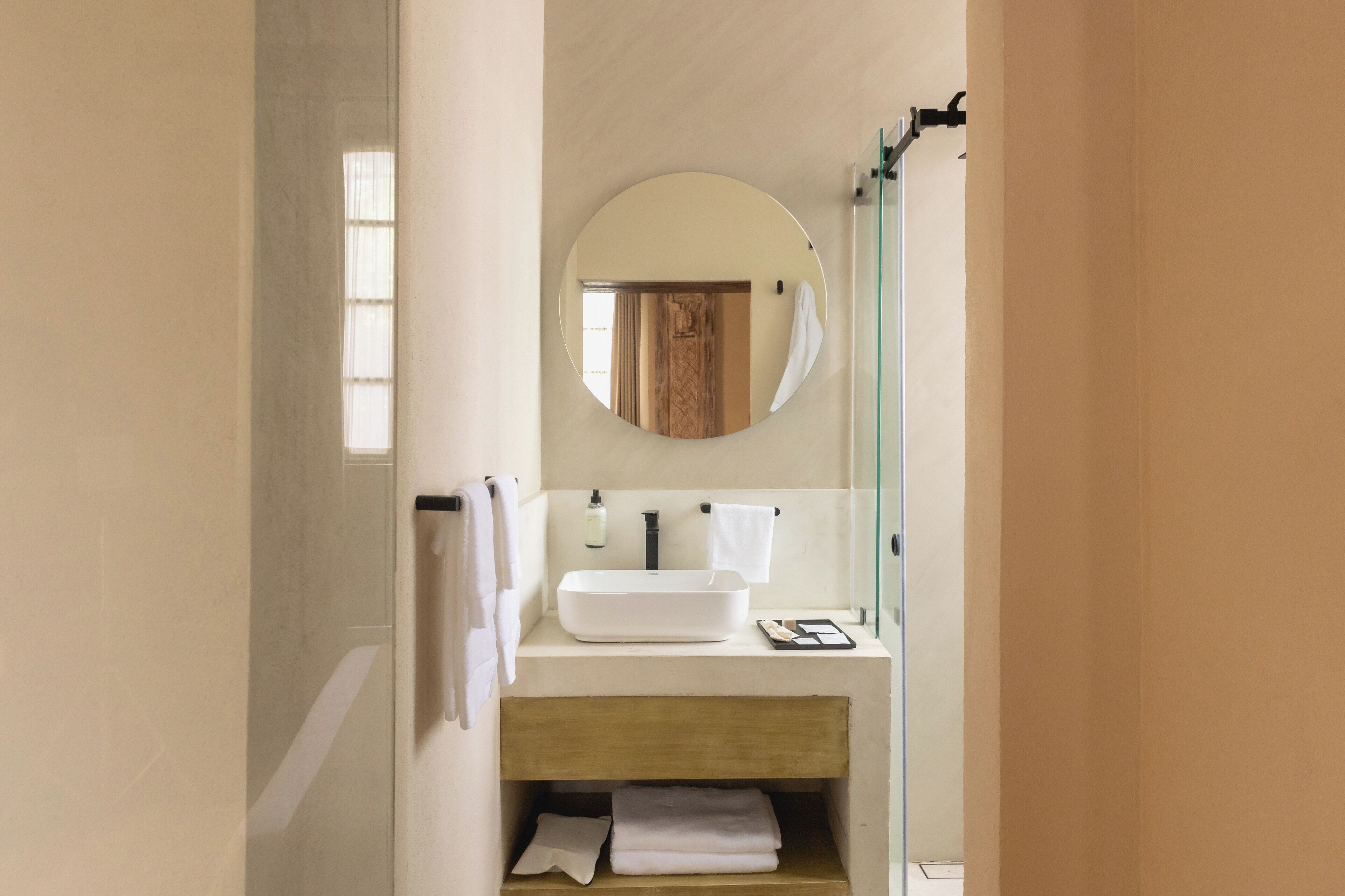 A modern bathroom with a round mirror, white sink, and wooden vanity.