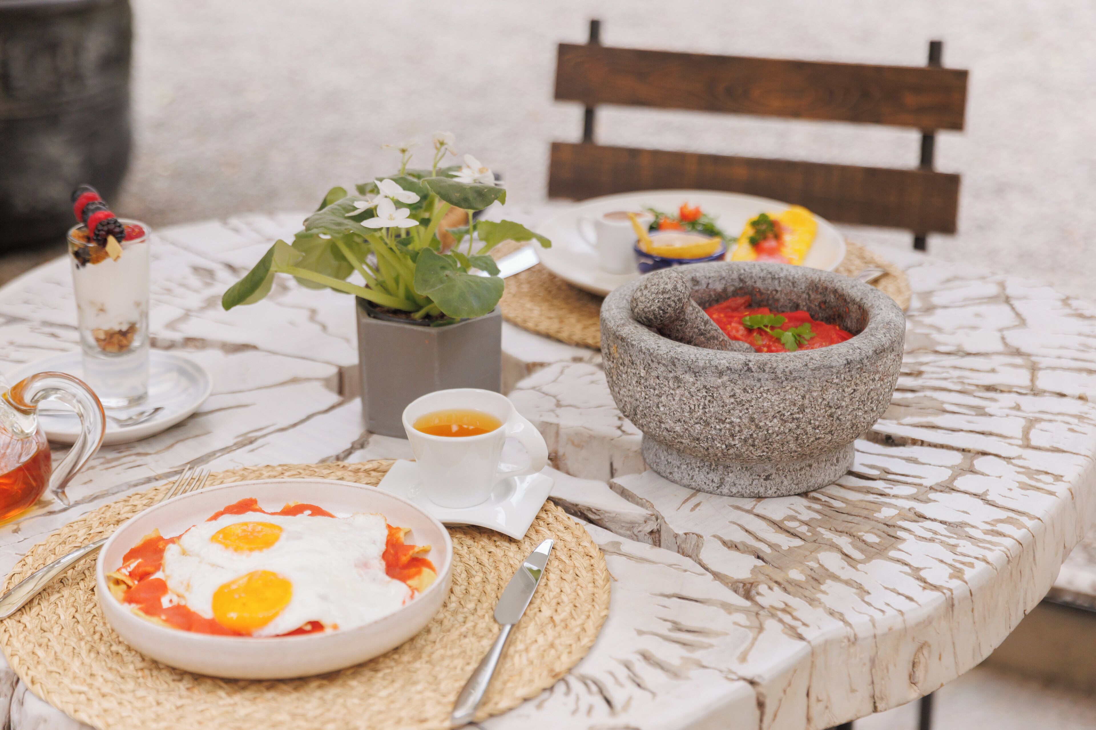 Uma mesa com itens de café da manhã, incluindo ovos, uma tigela de sopa, uma xícara de chá e uma planta.
