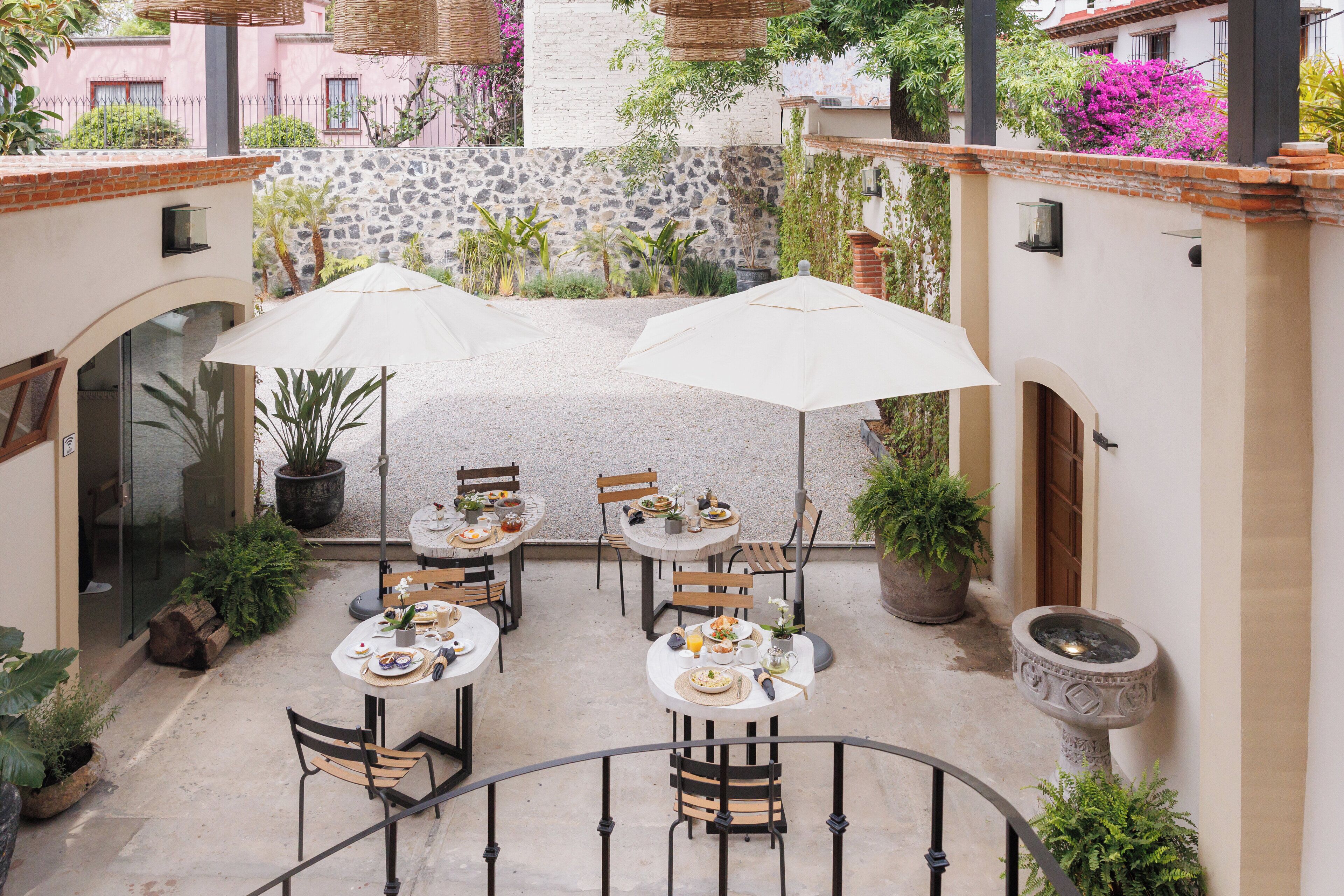 An outdoor patio with tables and chairs, surrounded by potted plants and a stone wall.