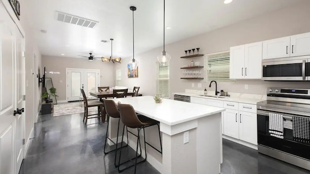 Una cocina moderna con una isla central, armarios blancos y electrodomésticos de acero inoxidable.