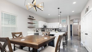 Una cocina moderna con armarios blancos, una isla central y un comedor con mesa y sillas de madera.
