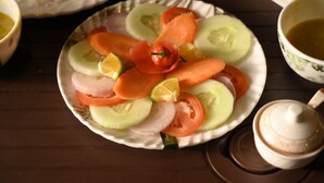 A plate of sliced vegetables including cucumbers, tomatoes, and onions, with a small chili pepper on top. - Bayaroo Stay Lamahatta (Darjeeling)