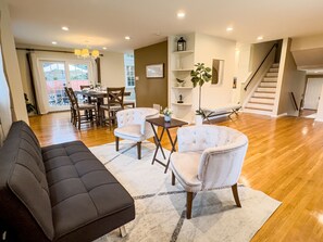 A spacious living area with a dark sofa, white armchairs, and a dining table. - Grand Lakeview Retreat Near Town • Game Rm • 4BR (Princeton)