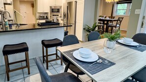 A modern kitchen with white cabinets, a stainless steel refrigerator, and a microwave. There is a dining area with a wooden table set for four, including plates, bowls, and cutlery. - Grand Lakeview Retreat Near Town • Game Rm • 4BR (Princeton)