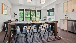 A modern kitchen with wooden cabinets, a dining area with a table and chairs, and large windows offering a view of the outdoors. - Alpine Adventure Pt C201 | Ski Escape | Powder Mtn (Eden)