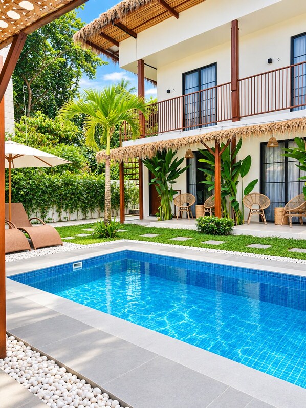 A two-story building with a swimming pool, outdoor seating, and tropical landscaping.