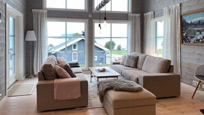 A spacious living room with a large window, a sofa set, a coffee table, and a painting on the wall. - 4 bedroom nice home in Hildre (Hildre)