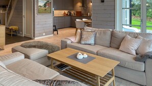 A modern living room with a sofa, a coffee table, and a dining area with chairs. - 4 bedroom nice home in Hildre (Hildre)