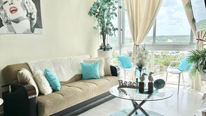 A modern living room with a sofa, a glass coffee table, and a view of the city through large windows. - Luxury Penthouse DGM Resort at Boca Chica  (Boca Chica)