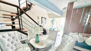 A modern living room with a glass-top coffee table, white upholstered chairs, a staircase, and a view of the outdoors. - Luxury Penthouse DGM Resort at Boca Chica  (Boca Chica)