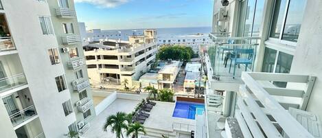 A high-rise building with a rooftop pool, multiple balconies, and a view of the sea.