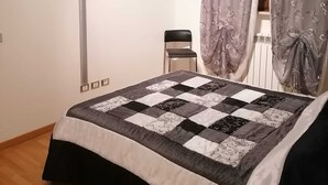 Ein Schlafzimmer mit Bett, Flachbildfernseher an der Wand, einem Sessel und einem Fenster mit Vorhängen.