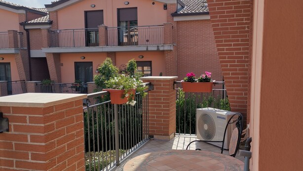 Ein Balkon mit Fliesenboden, einem runden Tisch, einem Stuhl aus Metall, Topfpflanzen und einer Samsung-Klimaanlage.