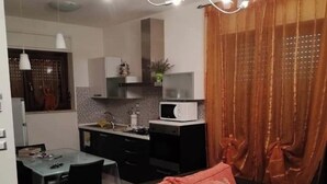 Ein modernes Wohnzimmer mit einer schwarzen Couch, einem Esstisch und einer Küchenzeile mit einer Mikrowelle.