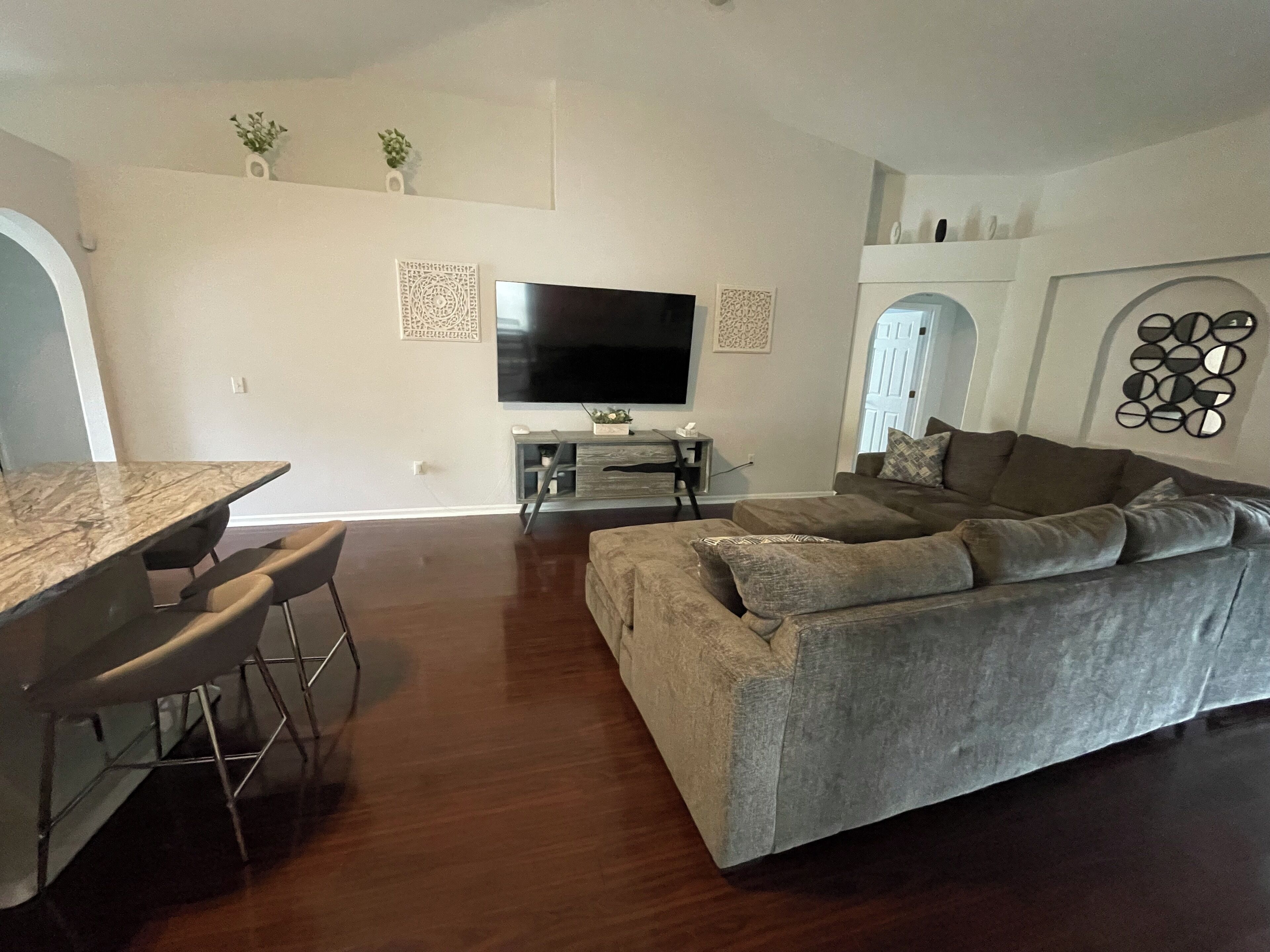 A living room with a grey sofa, a dining table with chairs, a flat-screen TV, and decorative wall art.