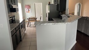 A kitchen with dark cabinets, a marble countertop island, and a dining area with a chair and table. - Tampa Bay Large Vacation Home (Ruskin)