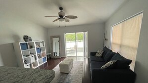 A living room with a dark grey sofa, a white coffee table, a marble bench, a white shelving unit, and a ceiling fan. - Tampa Bay Large Vacation Home (Ruskin)