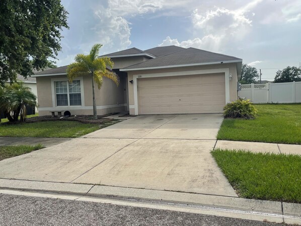 A single-story house with a garage, a front lawn, and a palm tree.
