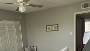 Une chambre à coucher avec un lit, un ventilateur de plafond, une porte et un tableau encadré au mur.