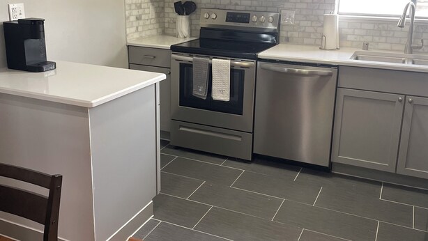 Une cuisine moderne dotée d’un îlot central, d’appareils électroménagers en acier inoxydable et d’un plancher à motifs en chevrons.