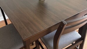 Une table de salle à manger rectangulaire en bois, accompagnée de quatre chaises, chacune dotée d’un siège rembourré. Un bol blanc contenant une plante verte est posé sur la table.