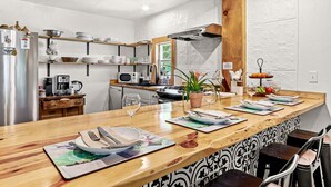 A kitchen with a wooden countertop, shelves with dishes, a refrigerator, and a microwave.