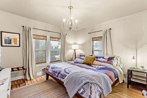 Une chambre à coucher avec un lit, des tables de chevet, un lustre, une lampe et des fenêtres équipées de stores.