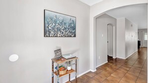 En hall med en stor blomstermålning på väggen, ett träbord med en korg och en inramad tavla, och ett klinkergolv.