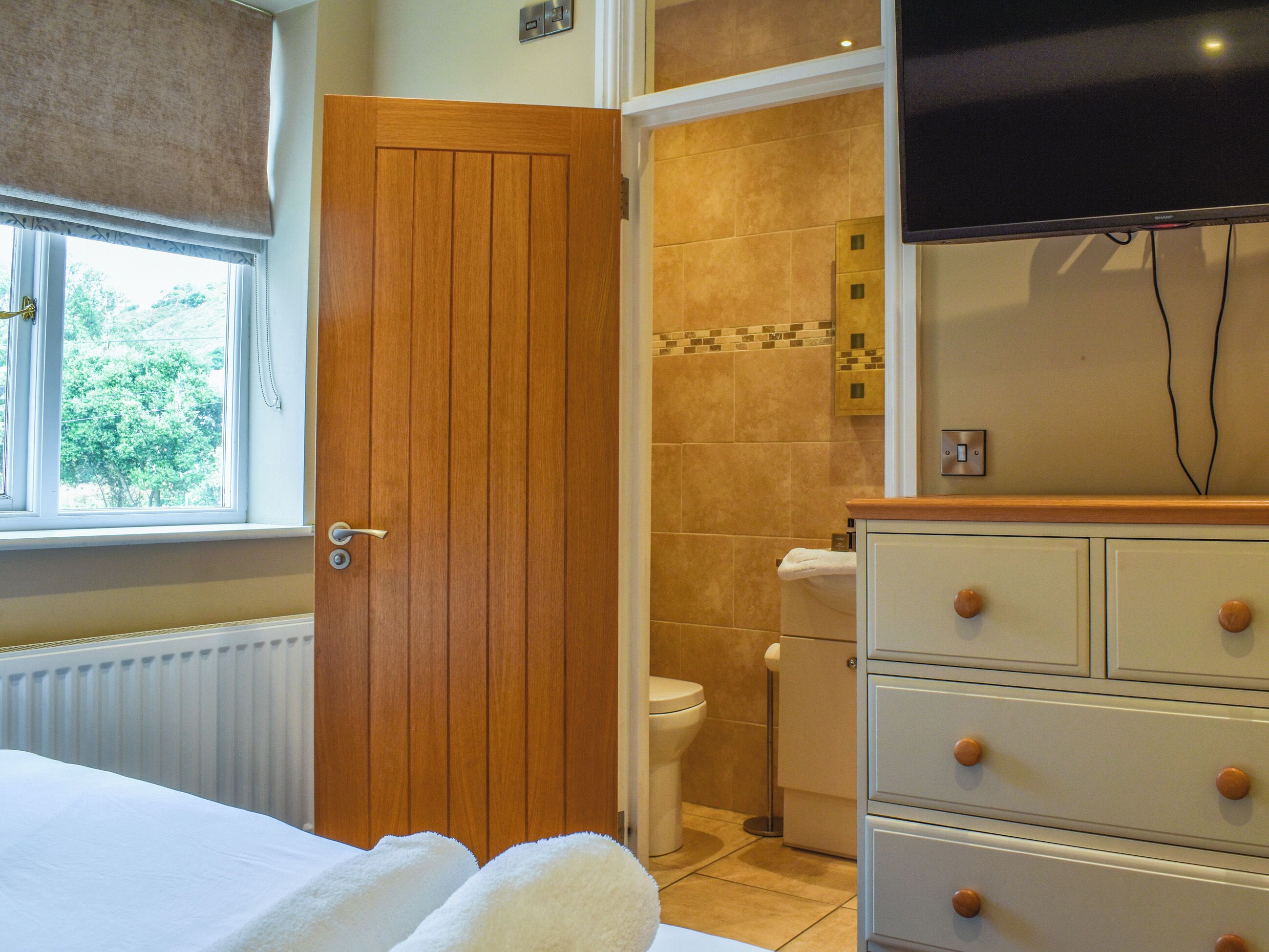 Een hotelkamer met een houten deur, een witte radiator, een wit bed, een witte dressoir en een televisie aan de muur.