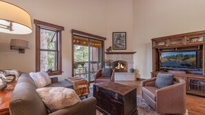 Una sala de estar acogedora con chimenea, asientos cómodos, televisor y ventanas amplias que dan a vistas del exterior.