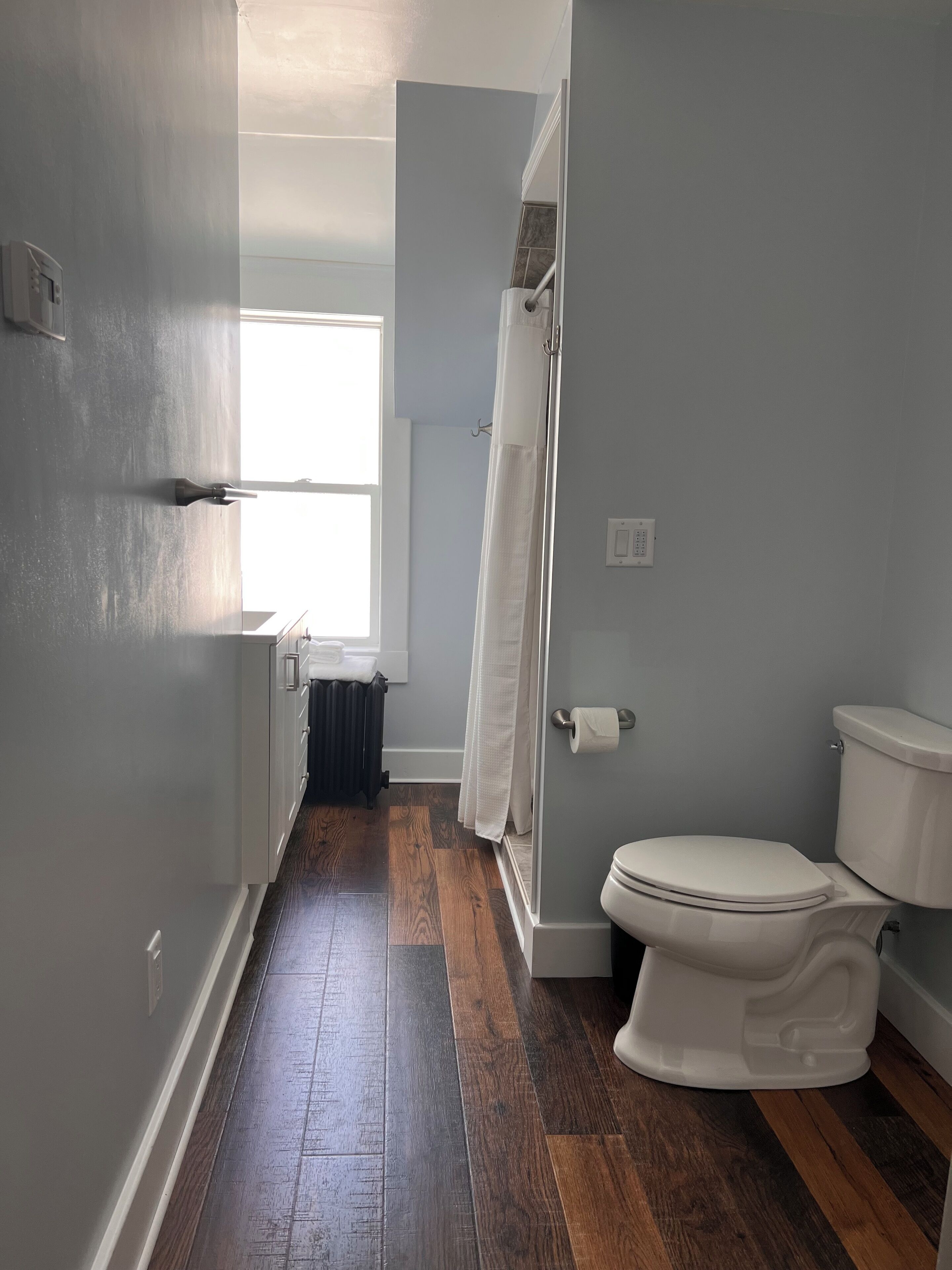 A narrow bathroom with a white toilet, a shower curtain, and a radiator.