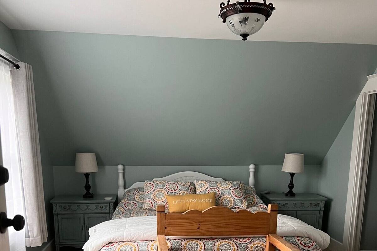 A bedroom with a bed, two nightstands, a wooden chair, and a ceiling light fixture.