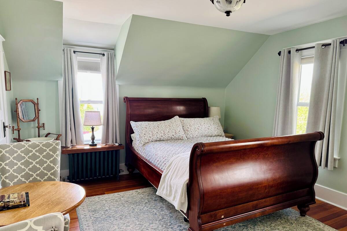 A bedroom with a wooden bed, a bedside table with a lamp, a chair, and a patterned rug.