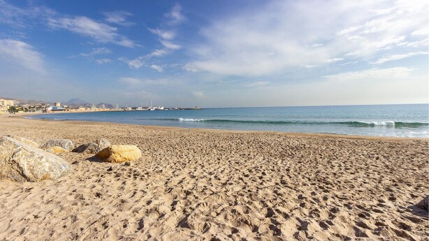 A wide sandy beach with visible footprints and large rocks.