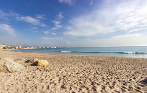 Une vaste plage de sable où l’on peut voir des empreintes et de gros rochers.