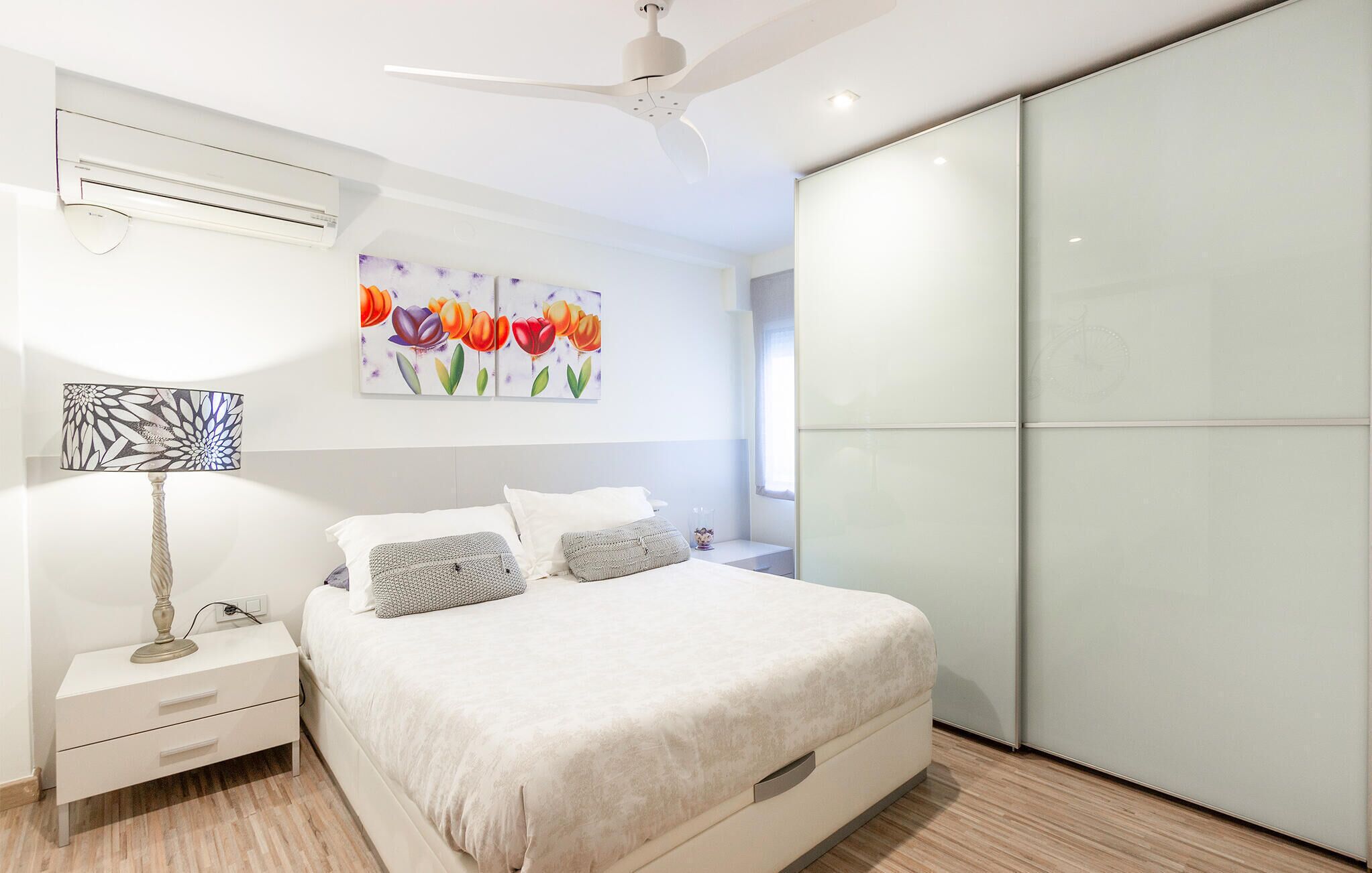 Ein modernes Schlafzimmer mit Bett, Nachttischen, Deckenventilator und einem großen Fenster.